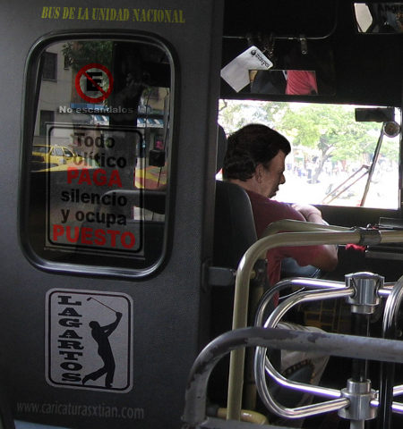 Aparece Juan Manuel Santos manejando un bus. Detrás de su silla de conductor, en la cabina aparecen las leyendas 'No escándalos', 'Todo político PAGA silencio y ocupa PUESTO', 'Lagartos (con la silueta de un golfista)'